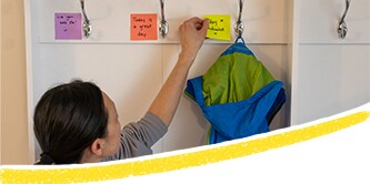 Mama klebt bunte Post-it® Notes mit positiven Botschaften neben Haken im Flur
