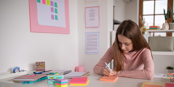 Ein Schüler macht sich Notizen auf Post-it® Notes in einem Lernbereich mit verschiedenen Büroartikeln, darunter Post-it® Notes und Notizbücher
