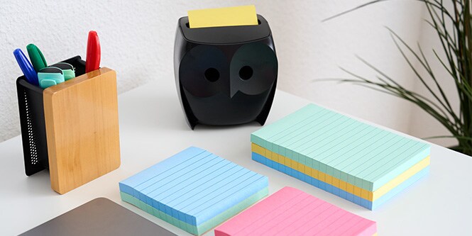 Ein Schreibtisch mit Post-it® Notes in verschiedenen Farben, ein Stifthalter und ein schwarzer Post-it® Note Dispenser in Eulenform
