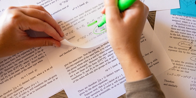 Schüler markieren Text auf Druckseiten mit einem Textmarker und transparenten Post-it® Notes, wobei sie sich auf mathematische Gleichungen konzentrieren.
